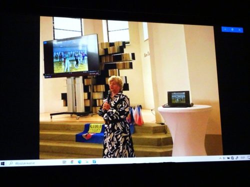 Na spotkaniu w Czerwonym Kościele Pani Prezes prezentuje seniorom z Czech nasz UTW