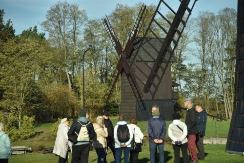 Sekcja fotograficzna zasłuchana w opowieści gospodarza, w tle wiatrak Leon